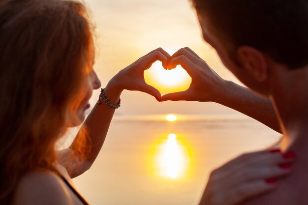 Free photo young sexy romantic couple in love happy on summer beach together having fun wearing swim suits showing heart sign on sundet